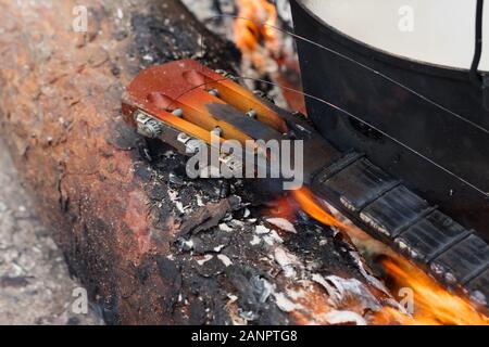 Registro di pino, bruciando il collo della chitarra e vecchio calderone di fuliggine su falò in foresta Foto Stock