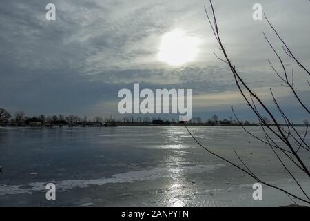 Il sole è coperto da alcune nuvole e riflette sul foglio di ghiaccio di un fiume ghiacciato nell'inverno 2019 2020 Foto Stock