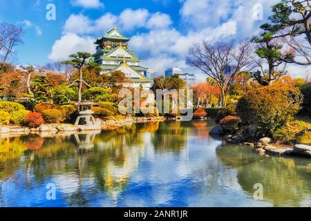 Bellissimo il Castello di Osaka in mezzo al verde autunnale di giardino con laghetto che riflette i colori della tradizionale architettura giapponese e cielo blu. Foto Stock