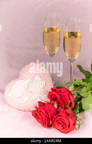 Il giorno di San Valentino card, due bicchieri di champagne su un sfondo rosa rose rosse e un cuore rosa, una candela accesa. Foto Stock