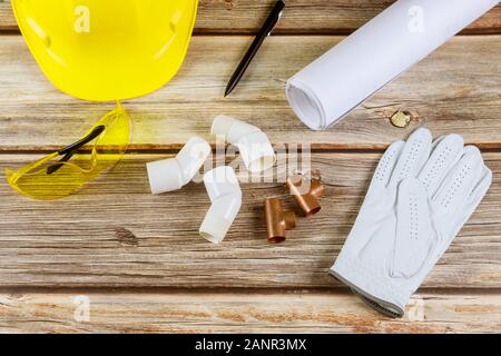 Business sito in costruzione, lavorando con blueprint in ufficio in rame tubo acqua guanti di protezione casco di sicurezza bicchieri sulla tavola di legno Foto Stock