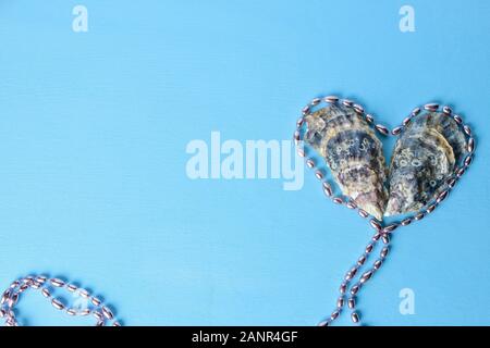 due gusci di ostriche si trovano nella forma di un cuore su uno sfondo blu.contorno cuore fatto da perle rosa. copia spazio Foto Stock