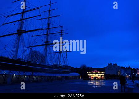 Luci di una giostra incandescente in inverno il crepuscolo scompaiono di fronte alla silhouette del nearcy Cutty Sark, Greenwich, Inghilterra. Foto Stock