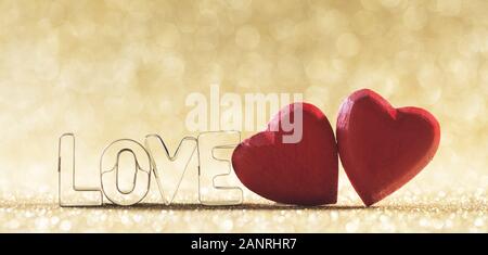 Due rossi in legno fatti a mano il cuore e la parola amore su golden luminose luci glitter sfondo bokeh di fondo Foto Stock