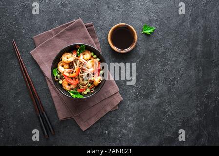 Stir fry con la sua pasta di soba, gamberi (gamberetti) e verdure. Asian cibo sano, pasto, STIR FRY nella ciotola con bacchette su sfondo nero, copia spac Foto Stock