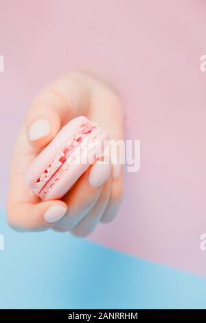 Elegante alla moda manicure femmina su sfondo rosa. Ragazza tiene per mano macaron cookies attraverso il foro Foto Stock