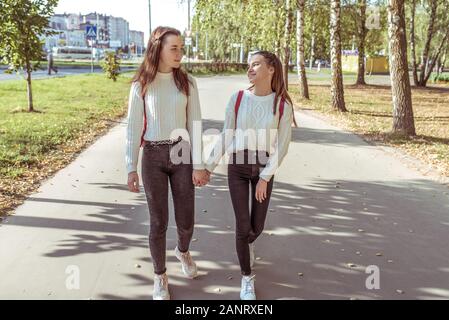 2 ragazze, studentesse, ragazzi 13-15 anni, giorni di autunno, estate in città a piedi a mano, sorridenti. Divertimento e piacere amiche. Essi Foto Stock