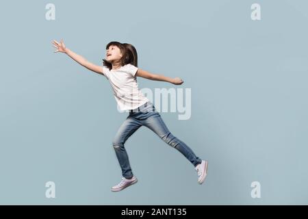 Piccolo felice ragazza di età prescolare saltando su sfondo blu. Foto Stock