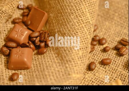 Cioccolatini e chicchi di caffè su uno sfondo di homespun ruvida stoffa. Close up Foto Stock