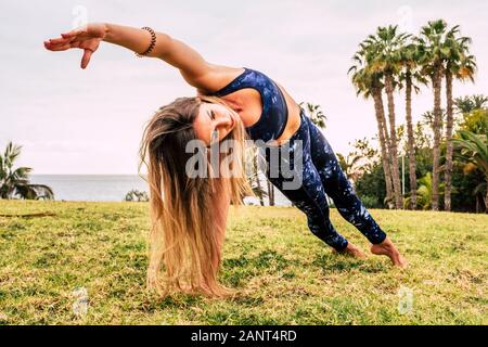 Uno stile di vita attivo persone concetto con bellissimi capelli lunghi biondi giovane donna facendo pilates equilibrata posizione sul verde prato naturale in outdoor spo Foto Stock