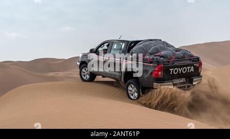 toyota hulux revo arrampicata una duna di sabbia che spruzzi sabbie intorno a dasht e lut o sahara deserto Foto Stock