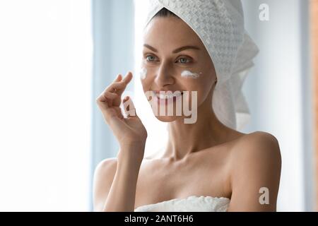 Bella donna con sorriso sano l'applicazione di crema sulle guance Foto Stock