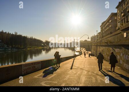 Vista la retroilluminazione dei Murazzi del Po in riva al fiume con gente che cammina in una soleggiata giornata invernale, Torino, Piemonte, Italia Foto Stock