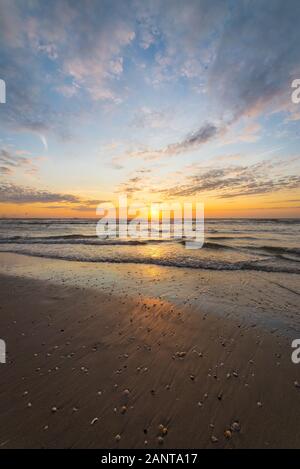 Il sole si trova all'orizzonte sul mare. Bellissimi colori nel cielo e riflessi in acqua e in sabbia bagnata. Foto Stock