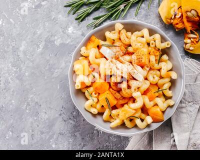 Fusilli con zucca, rosmarino e formaggio brie. Idea ricetta pasta. Cibo vegetariano. Pasta fatta in casa il piatto in grigio coppa sopra di cemento grigio Sfondo. Copia dello spazio. Vista superiore piatta o laici. Foto Stock