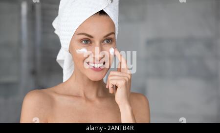 Colpo alla testa sorridente donna bella con una pelle perfetta applicazione di crema di latte Foto Stock