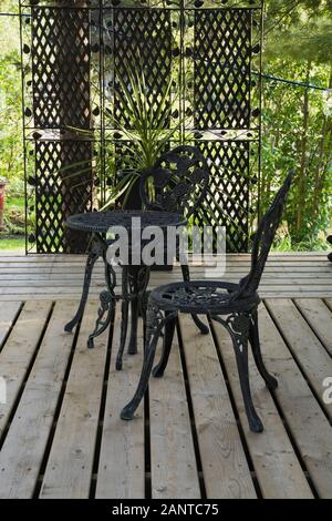 Nero ghisa metallo bistrot stile antiche sedie e tavolo rotondo sul terrazzo patio in legno davanti cortile giardino di campagna in estate Foto Stock