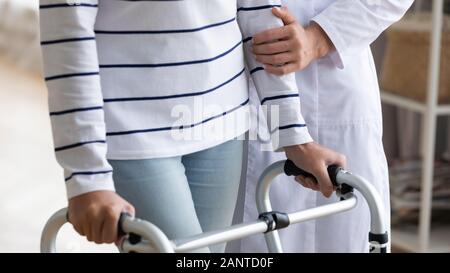 Chiudere l'infermiera aiutando disabilitato donna più anziana di utilizzare walker Foto Stock