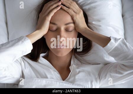 Vista superiore premuto donna che soffre di mal di testa, giacenti nel letto Foto Stock