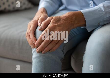 Vicino la donna più anziana toccando ginocchio con le mani, sensazione di dolore Foto Stock