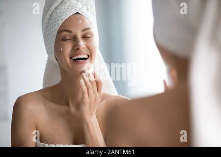 Felice bella donna di applicare la crema sulla faccia nella stanza da bagno Foto Stock