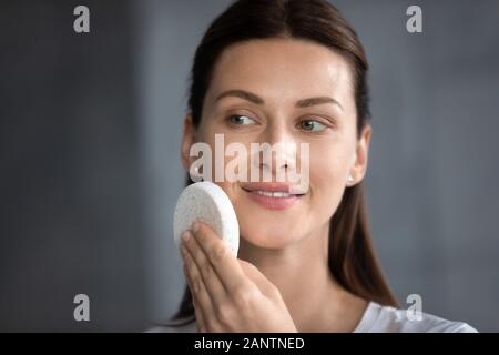 Colpo alla testa donna sorridente pulire la pelle con la pulizia del viso spugna Foto Stock