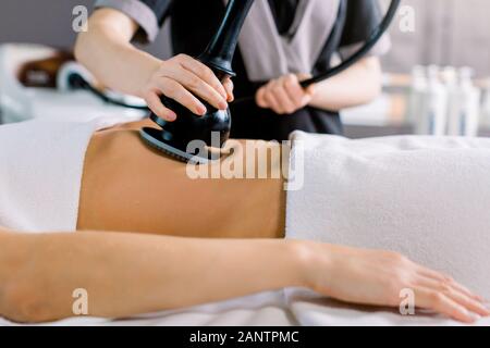 Tagliate il colpo di mano di cosmetologo facendo la cavitazione ad ultrasuoni la procedura sul ventre della donna. Irriconoscibile donna getting anti-grasso al trattamento Foto Stock