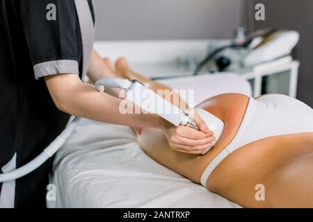 Medico donna cosmetologo rullo facendo massaggi con apparecchiatura sul client femmina cosce, vicino. Massaggio a rullo in Medical Spa Centre Foto Stock