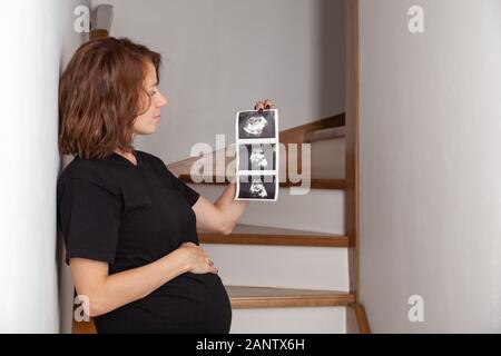 Ricci incinta Donna che guarda il suo bambino ecografia. Felice di attesa lady godendo la prima foto del suo bambino, anticipando la sua vita futura, copia Foto Stock