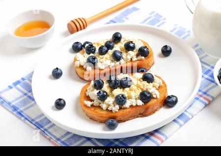 Panini con formaggio spalmabile, mirtilli e miele sulla piastra bianca Foto Stock