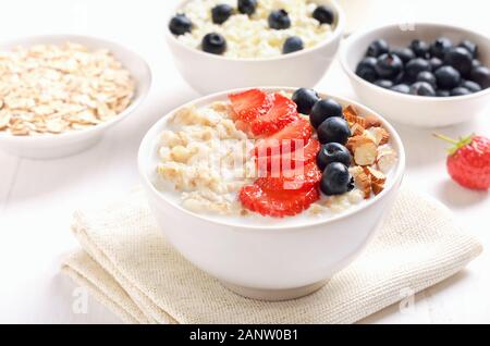 Farina di avena porridge con fette di fragole, mirtilli e i dadi nella ciotola sul tavolo bianco Foto Stock