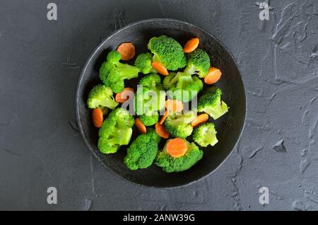 Broccoli e carote in padella in pietra nera di sfondo, vista dall'alto Foto Stock