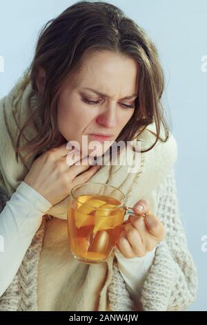 Malati moderno medioevo massaia in rotolo maglione collo e cardigan azienda tazza di tè caldo con lo zenzero, succo di limone e il miele isolati in inverno la luce blu b Foto Stock