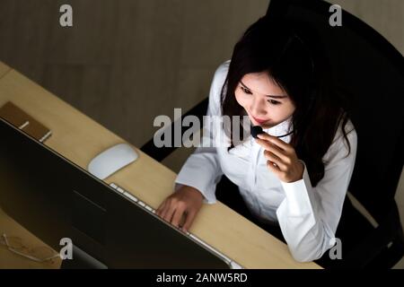 A tarda notte ambiente. Vista superiore del giovane adulto gentile operatore call center con cuffie lavorando di notte. Utilizzando per 24 h. 7 giorni di call center Foto Stock