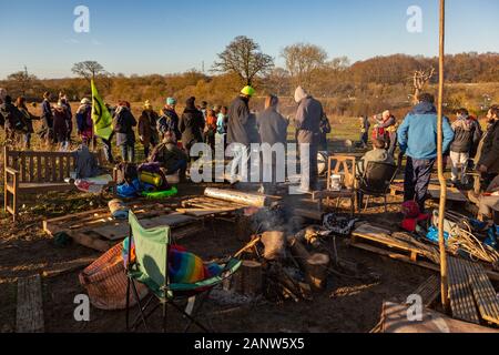 Harvil Road, Denham, Buckinghamshire, Regno Unito. 19 gennaio 2020. Una tranquilla comunità all'aperto con persone sedute su panchine e sedie di legno improvvisate intorno a un caminetto centrale; il fumo sale mentre zaini, coperte e oggetti personali si trovano nelle vicinanze. Diversi partecipanti si trovano sullo sfondo con delle bandiere, tra cui una bandiera verde con un simbolo. La scena sembra essere un'azione di protesta o ambientale locale collegata a HS2 a Harvil Road, ambientata in campi aperti sotto un cielo azzurro. Penelope Barritt/Alamy Live News Foto Stock