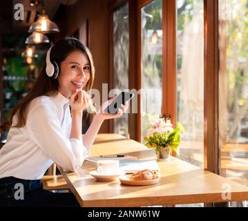 Femmina con successo i giovani adulti asian freelance che lavorano in cafe utilizzando il suo telefono cellulare e caffè set colazione. Foto Stock