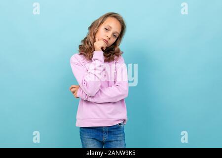 Bella scolaretta in blusa viola pensa a studiare isolato su sfondo blu Foto Stock