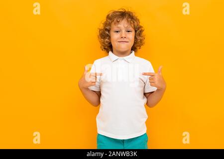 Ragazzino con capelli ricci in maglietta colorata e pantaloncini corti si mostra come isolato su sfondo giallo Foto Stock