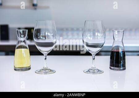 Vuoto due bicchieri di vino e una coppia di piccoli decantatori riempito con vini bianchi e rossi, gusto stemware su di un bianco luminoso con bancone bar della sala di degustazione Foto Stock