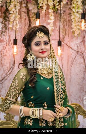 Ritratto di un indiano sposa in piedi con elegante vestito e gioielli con il trucco in una sala banchetti. La tradizione indiana sposa in matrimonio in Kolkata Foto Stock