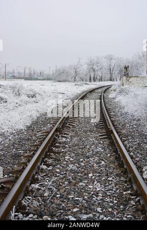Una linea ferroviaria che corre lungo una recinzione di cemento bianco che è coperta di neve bianca soffice in inverno. Foto Stock