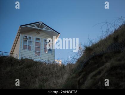 Una vista dal basso di uno chalet di vacanza posizionato precariosamente sulla scogliera a Hele Bay, Ilfracombe, Devon, Inghilterra a causa di erosione costiera Foto Stock