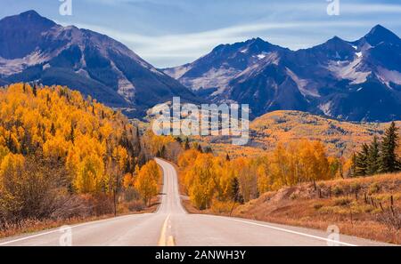 Un vuoto di Colorado Highway 145 nel mezzogiorno circondato da Autunno a colori nei pressi di Telluride, Colorado. Foto Stock