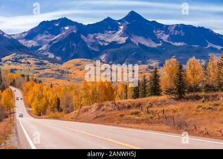 Veicoli viaggiano verso il basso Colorado Highway 145 nel mezzogiorno circondato da Autunno a colori nei pressi di Telluride, Colorado. Foto Stock