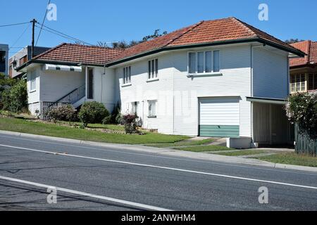 Norman Park, Brisbane, una grande casa in legno a due piani degli anni '1950 con tetto in piastrelle rosse e garage sotto casa e un parcheggio aggiuntivo, senza recinzione Foto Stock