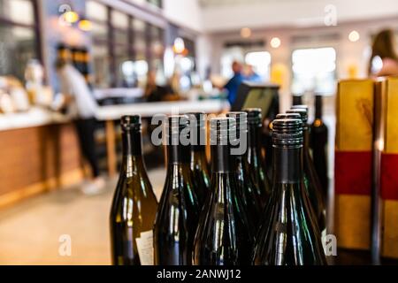 Le bottiglie di vino, scuro in vetro ambrato con tappo a vite nero guarnizione closeup messa a fuoco selettiva, persone che acquistano e degustazione dei vini in background Foto Stock