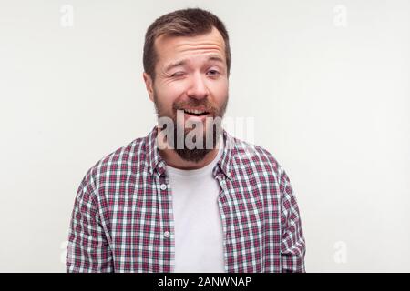 Ritratto di bello barbuto uomo positivo in plaid shirt sorridente e baluginare scherzosamente in telecamera con ottimismo espressione allegra, le rughe sul viso Foto Stock