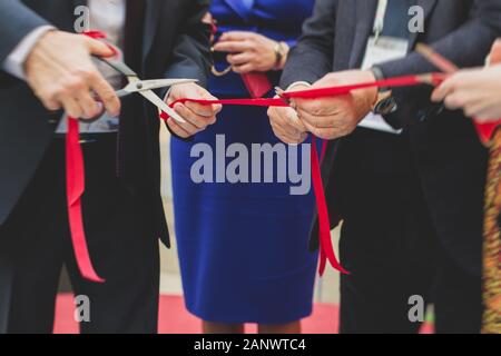 Processo di taglio il nastro rosso durante l'inaugurazione del nuovo centro commerciale Mall building, apertura della mostra, vista ravvicinata di ribbo rosso Foto Stock