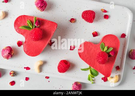 Vegano grezzo a forma di cuore o torte cheesecake con lamponi freschi, menta e fiori secchi. Il giorno di San Valentino dessert. cibo sano concetto. vista superiore Foto Stock