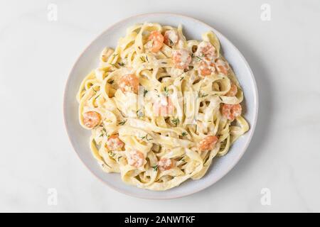 La pasta italiana Le fettuccine o tagliatelle in una salsa cremosa con gamberetti in una piastra su marmo bianco tavola. vista superiore Foto Stock